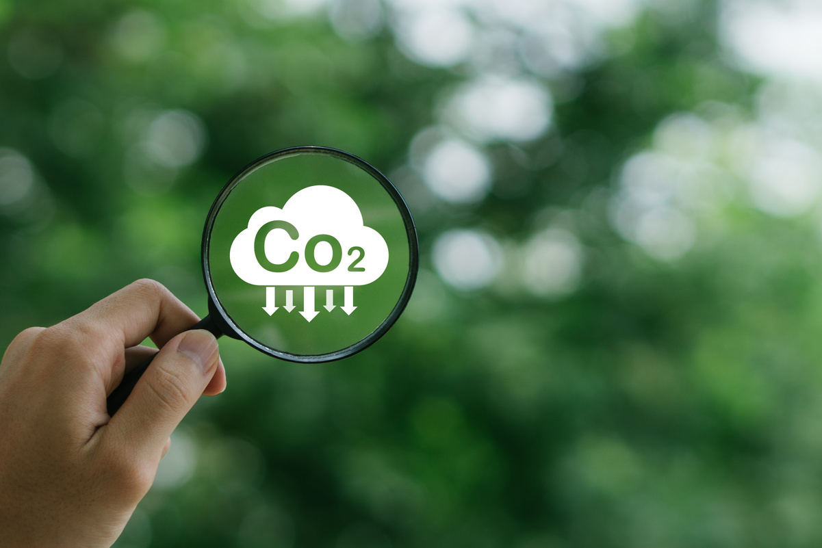 CO2 reducing icon inside magnifier glass on greenery background,global warming for environmental.Net zero and carbon neutral concept.